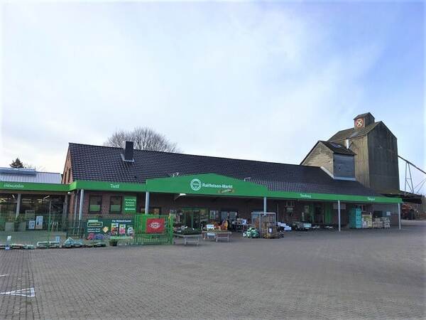 Du siehst den Raiffeisen Markt Rosengarten-Nenndorf mit grünem Vordach, Außenverkauf und altem Siloturm im Hintergrund.