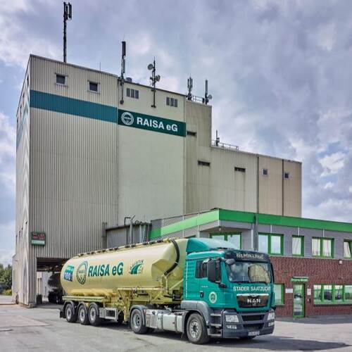 Du siehst ein Futtermittelwerk der RAISA eG mit einem grünen Silozug und Gebäuden im Hintergrund.