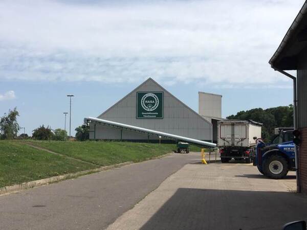 Du siehst eine große Lagerhalle der RAISA Geschäftsstelle Tönnhausen mit Förderband und LKW.