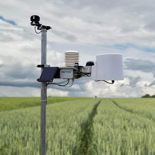 Du siehst eine digitale Wetterstation von METOS® auf einem Getreidefeld unter bewölktem Himmel.
