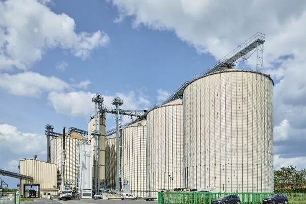 Du siehst ein großes Getreidesilo mit mehreren runden Silotürmen und Fördertechnik bei blauem Himmel.