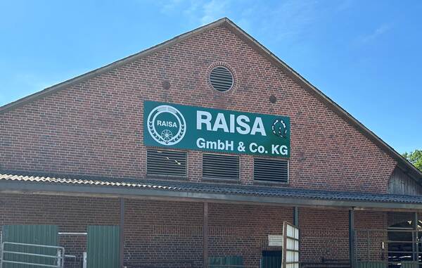 Du siehst ein Backsteingebäude mit grünem Firmenschild der RAISA GmbH & Co. KG an der Fassade.
