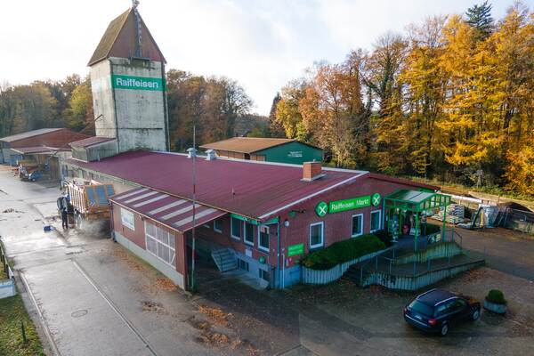 Du siehst einen Raiffeisen-Markt Axstedt mit rotem Dach, Lagergebäuden und Siloturm im herbstlichen Umfeld.