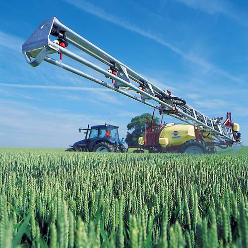 Du siehst einen Traktor mit Pflanzenschutzspritze bei der Feldarbeit in einem grünen Getreidefeld.