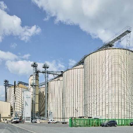 Du siehst ein großes Getreidesilo mit mehreren runden Silotürmen und Fördertechnik bei blauem Himmel.