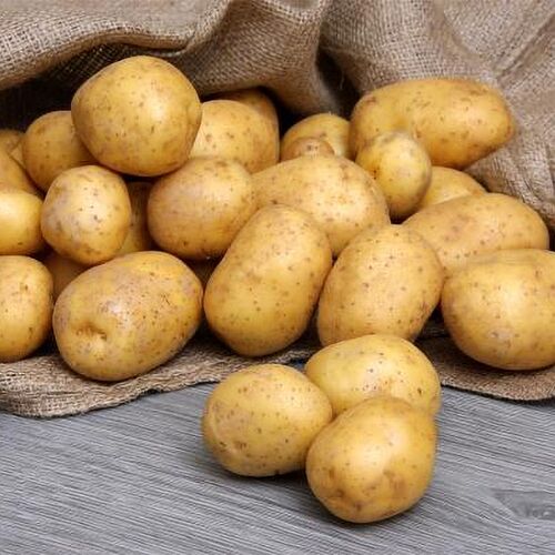 Du siehst frisch geerntete, saubere Kartoffeln, die aus einem Jutesack auf einen Holztisch rollen.