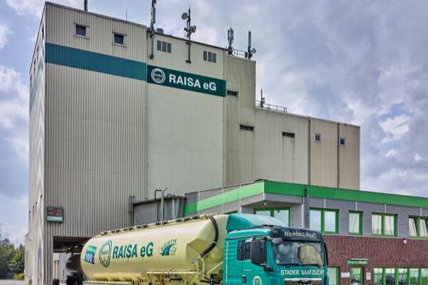 Du siehst ein Futtermittelwerk der RAISA eG mit einem grünen Silozug und Gebäuden im Hintergrund.